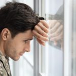 Depressed guy soldier looking through window at home